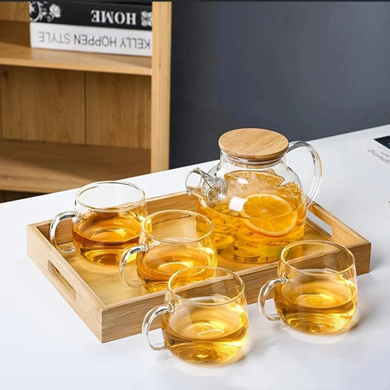 Ensemble théière en verre avec couvercle en bambou et quatre tasses transparentes disposées sur un plateau en bois