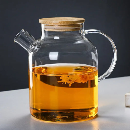 Théière en verre avec couvercle en bambou illuminée par éclairage doux, contenant une infusion dorée avec chrysanthème épanoui