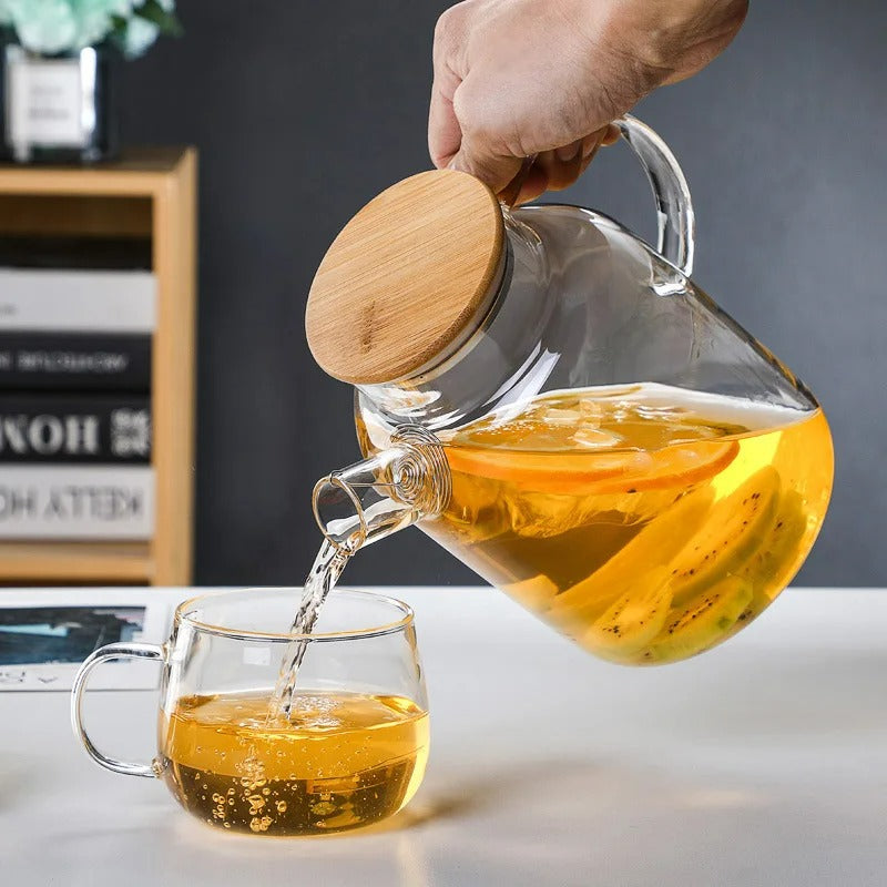 Théière en verre avec couvercle en bambou servant une infusion aux agrumes et kiwi dans une tasse transparente